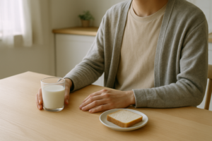 Persoon aan een lichte keukentafel met een glas melk, in gedachten over klachten na zuivel