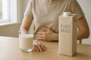 Pers die aan tafel zit met een glas koemelk en een plantaardig alternatief, en rustig nadenkt over wat het beste valt op de buik