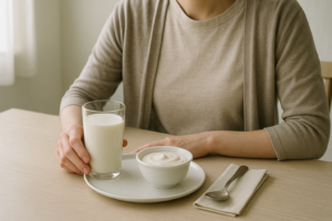 Persoon aan een lichte keukentafel die rustig naar een glas melk en een schaaltje yoghurt kijkt