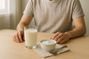 Glas melk en schaaltje yoghurt op een lichte keukentafel met handen op de achtergrond